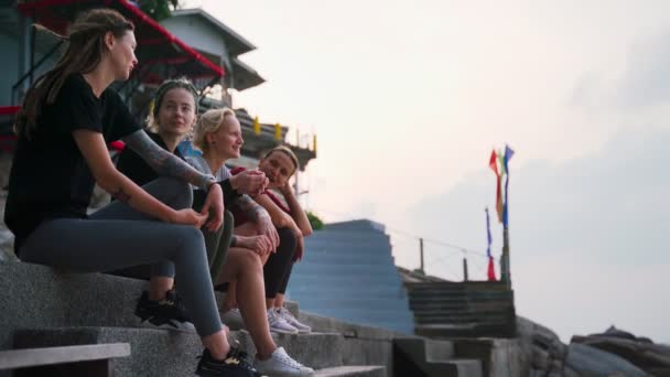 Grupo de cuatro mujeres jóvenes, mejores amigos sentados al aire libre y hablando . — Vídeos de Stock