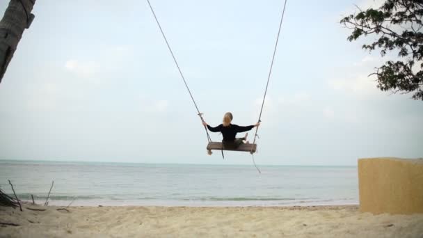 Jonge blonde vrouw swinging op grote schommels op het strand met een uitzicht op zee. — Stockvideo