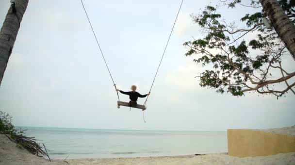 Giovane donna bionda che oscilla su grandi altalene sulla spiaggia con vista sul mare . — Video Stock