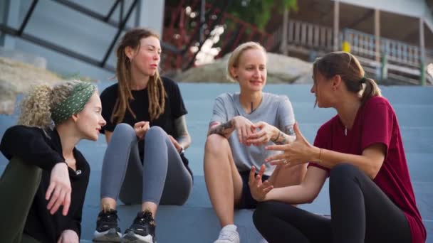 Groupe de quatre jeunes femmes, meilleurs amis assis en plein air et parlant . — Video