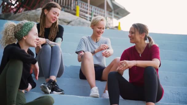 Grupo de cuatro mujeres jóvenes, mejores amigos sentados al aire libre y hablando . — Vídeo de stock