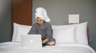 Young caucasian woman using a laptop while sitting on the bed in the hotel room