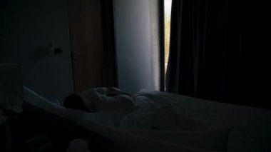 A young caucasian woman traveler wakes up and opens blackout curtains