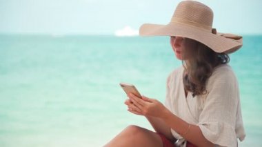 A young woman in a big straw hat using her smartphone