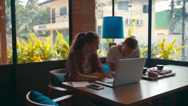 Два молодых сотрудника работают над ноутбуками и обсуждают бизнес — стоковое видео