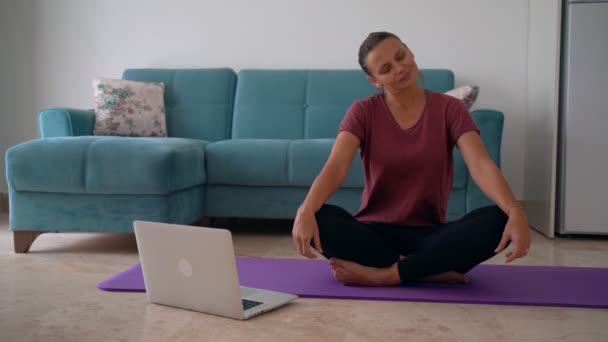 Atractiva joven haciendo yoga estirando yoga en línea en casa. — Vídeos de Stock