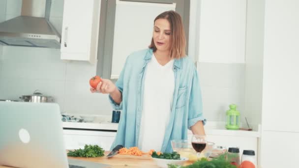 Молодая женщина готовит на кухне, разговаривая с друзьями через интернет . — стоковое видео
