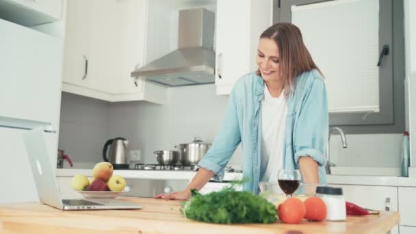 Jonge vrouw koken in de keuken tijdens het praten met vrienden via internet. — Stockvideo