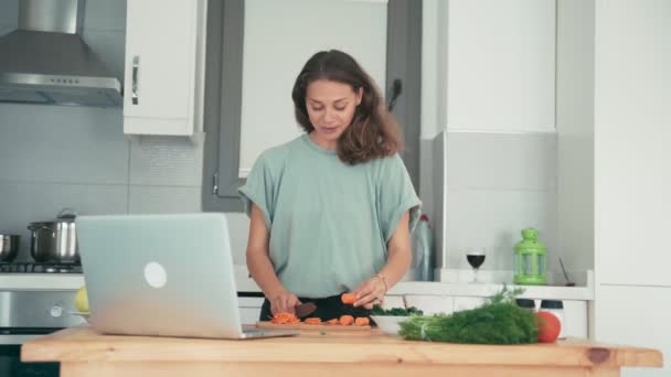 Mujer joven cocinando en la cocina mientras habla con amigos a través de Internet . — Vídeo de stock