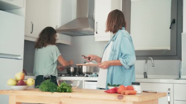 Dos mujeres jóvenes bastante caucásicas cocinando en la cocina brillante . — Vídeos de Stock
