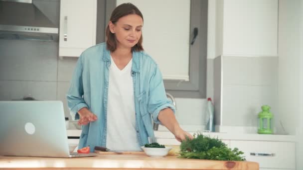Młoda kobieta gotuje w kuchni rozmawiając z przyjaciółmi przez internet. — Wideo stockowe