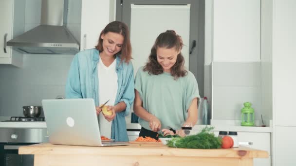 Twee jonge vrouwen dansen tijdens het koken en praten met vrienden via het internet — Stockvideo