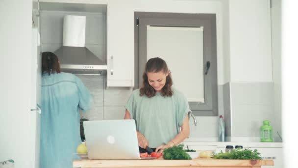 Twee jonge vrij blanke vrouwen koken in de lichte keuken. — Stockvideo