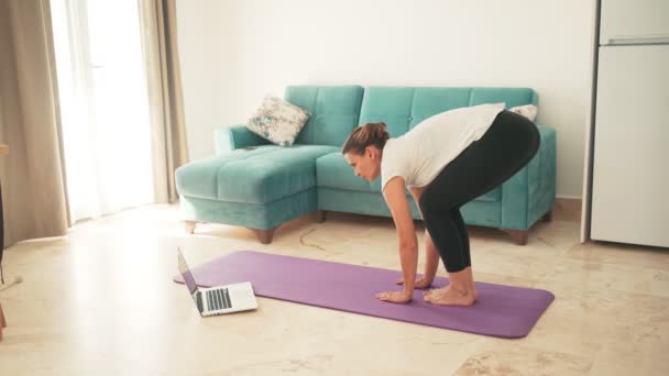Vonzó fiatal nő csinál jóga nyújtás jóga online otthon. — Stock videók