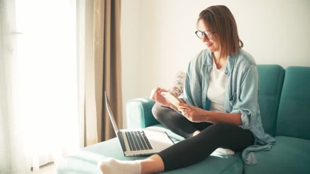Mladá žena pracuje doma s notebookem a smartphonem v obývacím pokoji. — Stock video