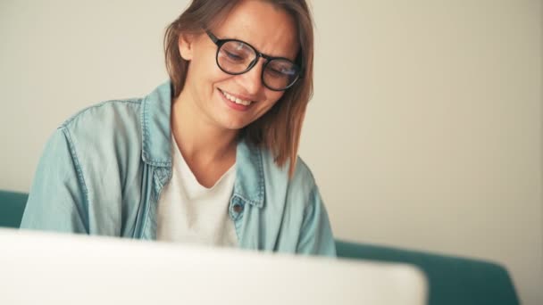Gözlüklü genç bir kadının laptopunu kullanarak evde çalışmasını yakından çek. — Stok video