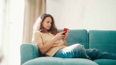 Akıllı telefonunu kullanan genç bir kadın, koltukta otururken bir mesaj yazıyor.