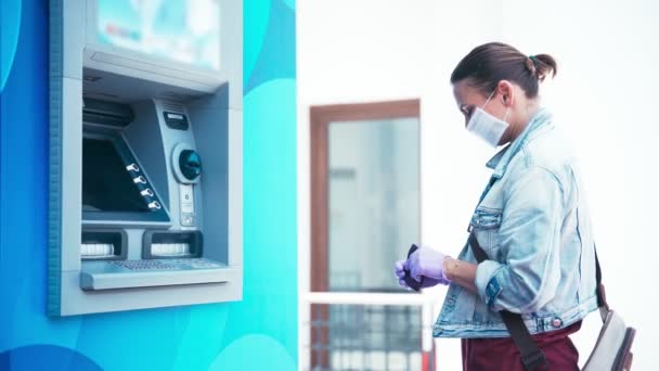 Mujer con una máscara médica y guantes de látex de protección llega a un cajero automático — Vídeo de stock