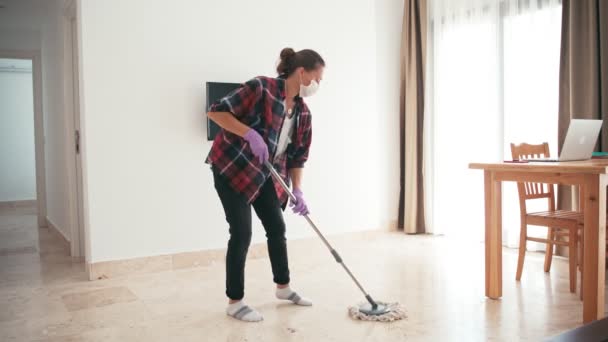 Μια νεαρή γυναίκα καθαρίζει το σαλόνι σφουγγαρίζοντας το πάτωμα κάνοντας δουλειές του σπιτιού. — Αρχείο Βίντεο