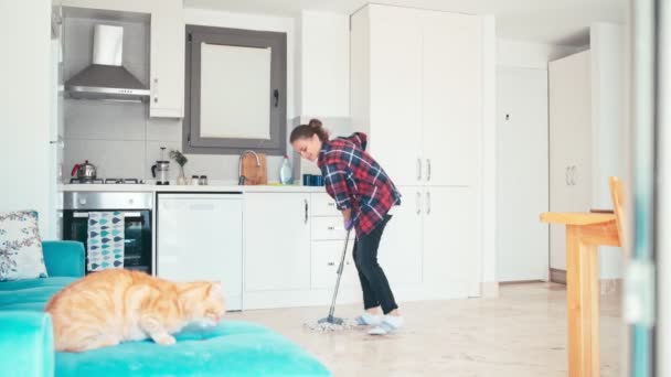 Een jonge vrouw maakt de woonkamer schoon en dweilt de vloer met huishoudelijk werk. — Stockvideo