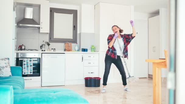 Een gelukkige jonge vrouw wast de vloer met dweilen en dansen in de keuken — Stockvideo