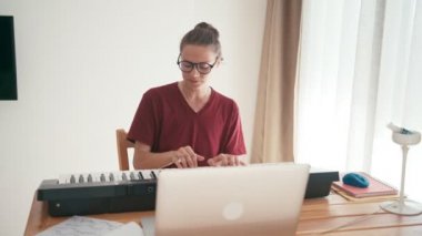 Genç bir kadın bilgisayarını kullanarak online piyano klavyesi çalıp şarkı söylüyor..