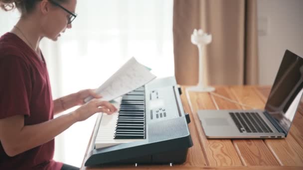 Ung kvinna lära sig piano med en online-kurs med hjälp av sin bärbara dator. — Stockvideo