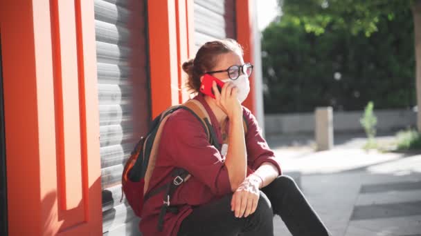 Una mujer joven con una máscara médica protectora y gafas usando su teléfono inteligente — Vídeos de Stock