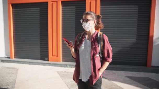 Une jeune femme portant un masque médical protecteur et des lunettes avec son smartphone — Video