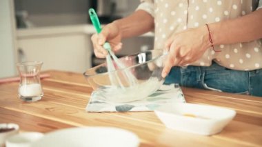 Bir kadın cam kasede çırpılmış yumurta beyazı çırpıyor ve şeker ekliyor.