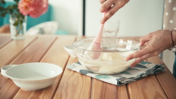 Kadınların elleri krema veya hamuru cam bir kasede silikon spatulayla karıştırıyor. — Stok video