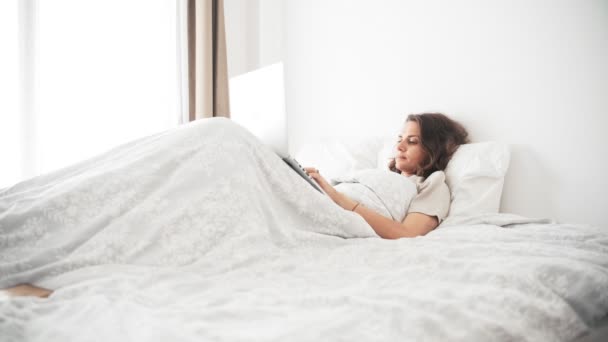 A young sleepy woman in pajamas working at home using her laptop — Stock Video