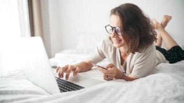 Bilgisayarını ve kredi kartını kullanarak online alışveriş yapan neşeli genç bir kadın.