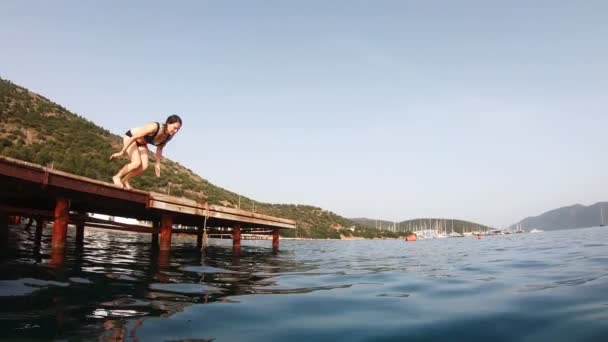 Plan au ralenti d'une jeune femme plongeant d'une jetée en bois vers une mer bleue claire — Video