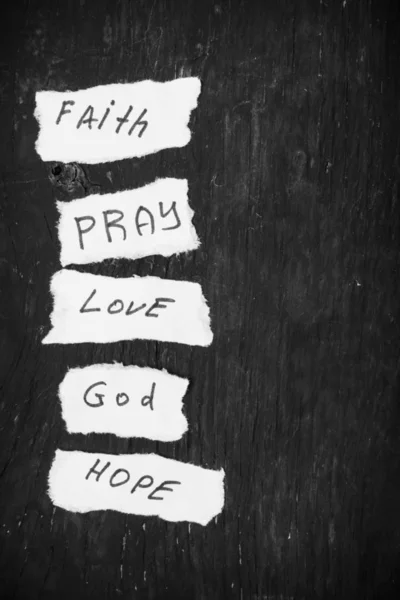Inskriptionen på vitt papper, tro, hopp, kärlek, Gud, be på en svart trä bakgrund. — Stockfoto