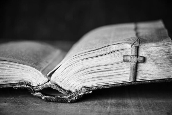 Cross on the Bible on a wooden background. Holy book. Black and white photography