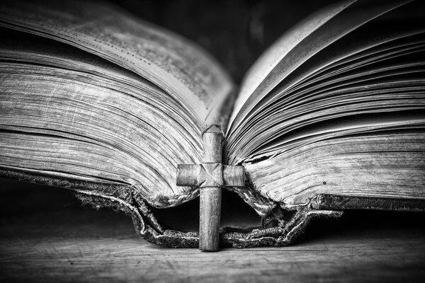 Cross on the Bible on a wooden background. Holy book. Black and white photography