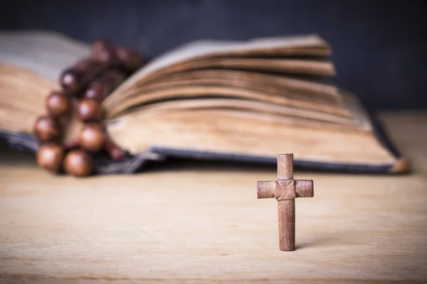 Cruz marrom e rosário sobre a Bíblia em um fundo de madeira. Livro sagrado . — Fotografia de Stock
