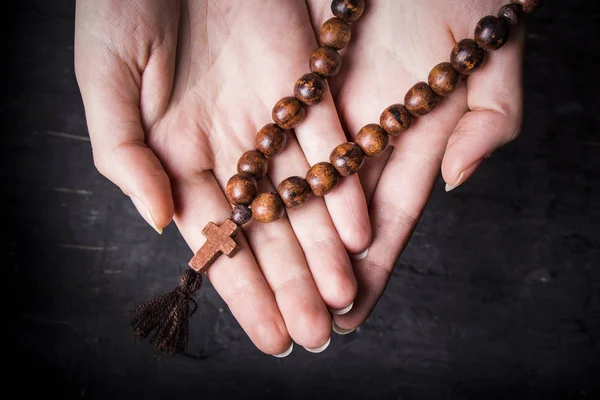 Rosaire et croix dans les mains féminines sur un fond sombre — Photo