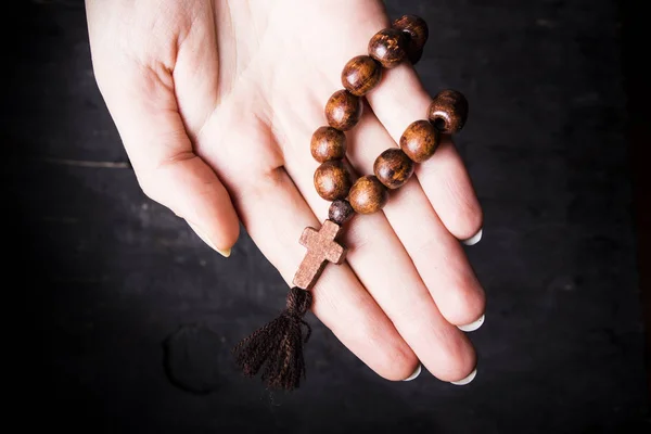 Rosaire et croix dans les mains féminines sur un fond sombre — Photo