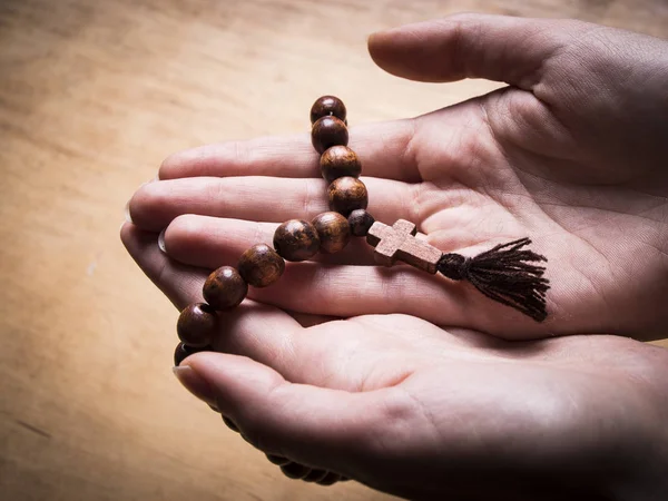 Rosaire et croix dans les mains féminines sur un fond en bois . — Photo