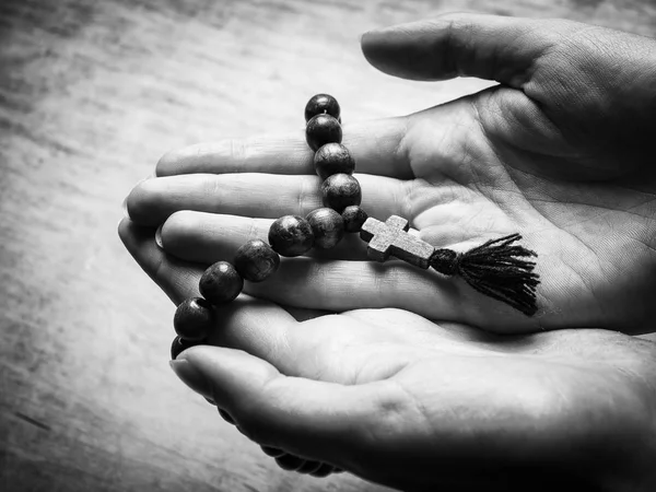 Rosaire et croix dans les mains des femmes sur un fond en bois. Photo noir et blanc . — Photo