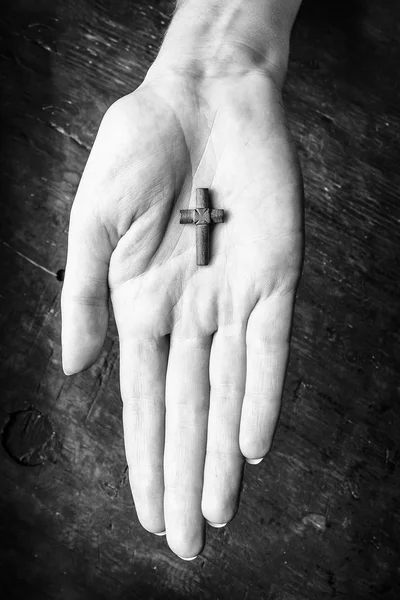 Cross in female hands on a wooden background. Black and white photo. — Stock Photo, Image