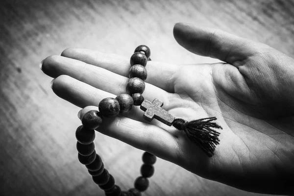 Tespih ve eller haç ahşap arka plan üzerinde. Siyah ve beyaz fotoğraf.