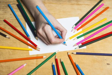 Ahşap masa çizmek için renkli kalemler kümesi. Bir yaprak kağıda kadın çizer