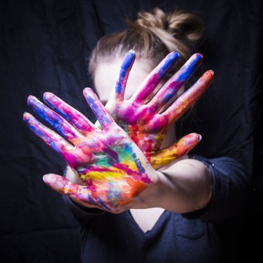 Sanatçı yüzünü elleri parlak renkli boya kapsar.