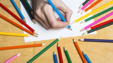 Ahşap masa çizmek için renkli kalemler kümesi. Bir yaprak kağıda kadın çizer