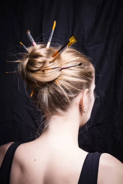 Die Künstlerin mit Pinseln im Haar auf dunklem Hintergrund — Stockfoto