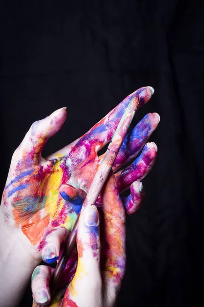 Manos del artista en pintura de color brillante con pincel sobre fondo negro . — Foto de Stock