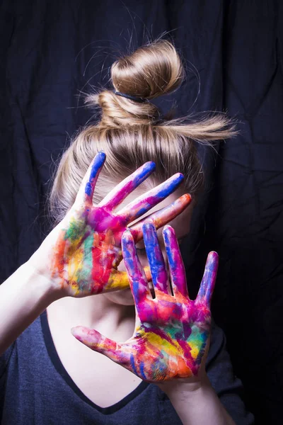 Sanatçı yüzünü elleri parlak renkli boya kapsar.